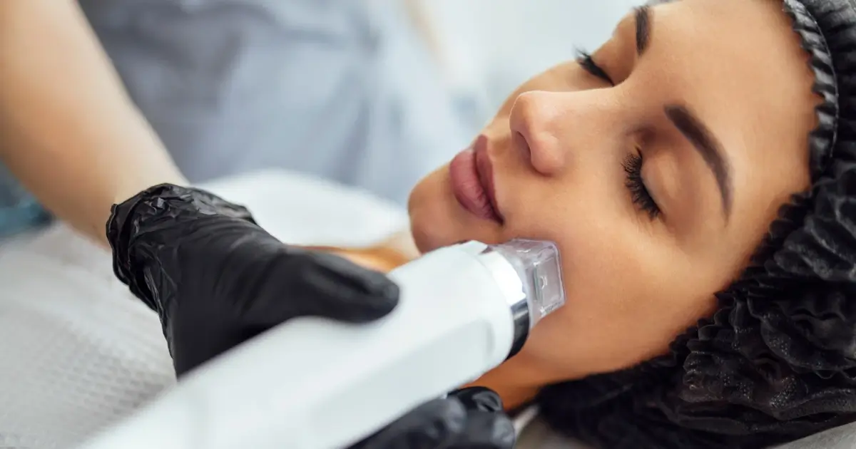 A woman receiving Morpheus8 RF microneedling treatment on her face, performed by a professional wearing black gloves, to tighten and rejuvenate her skin in Madisonville, LA